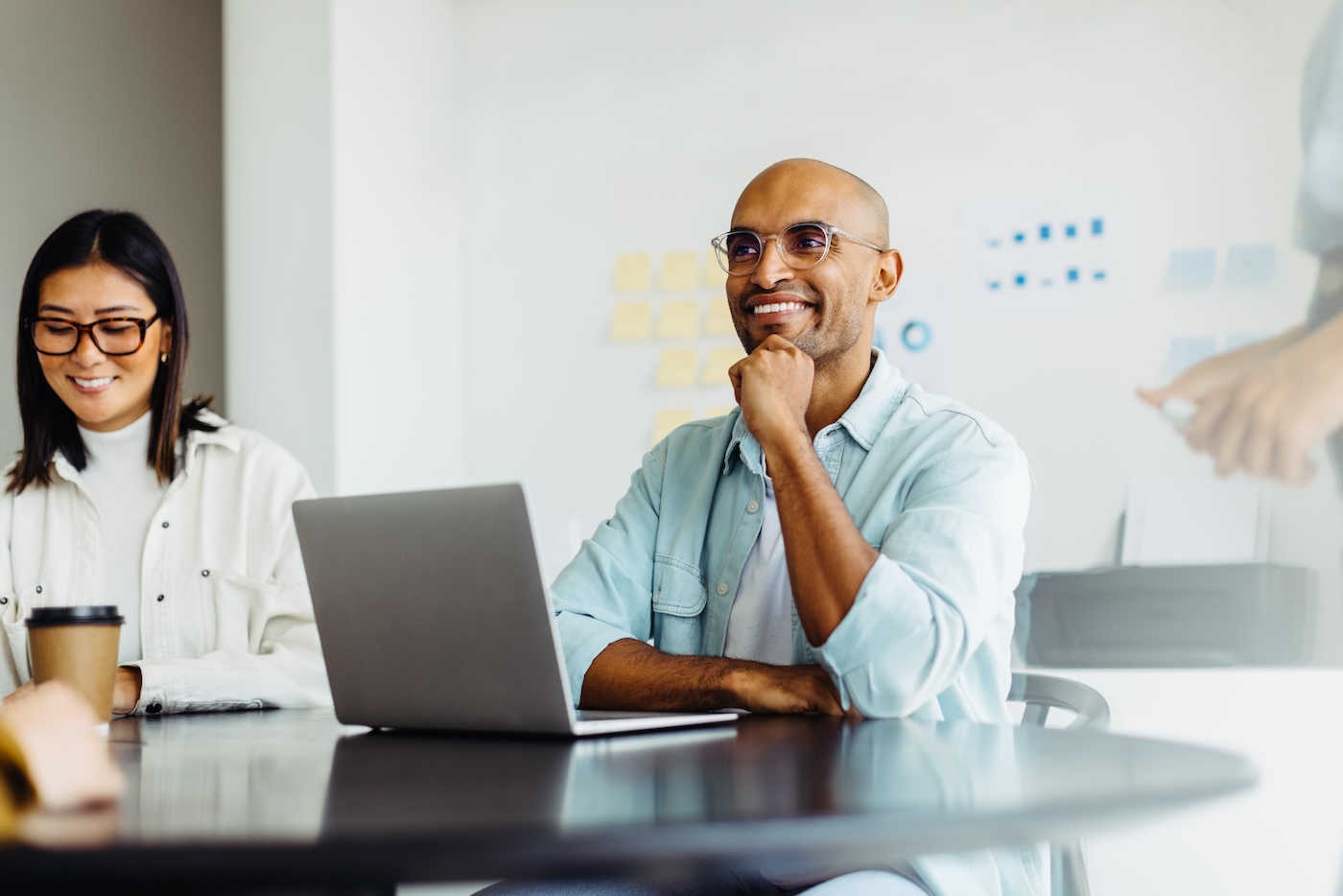 Business man listening to a discussion during a meeting with his team. Happy young designer sitting at a table with his colleagues in a creative office.